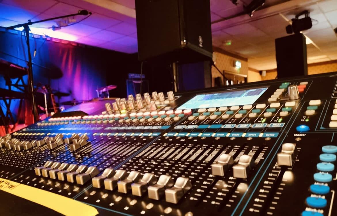 Digital mixing console with faders lit up at a live music venue
