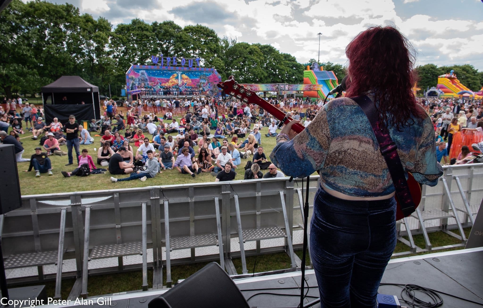 Guitarist on an outdoor festival stage looking out over a large summer crowd in Hertfordshire
