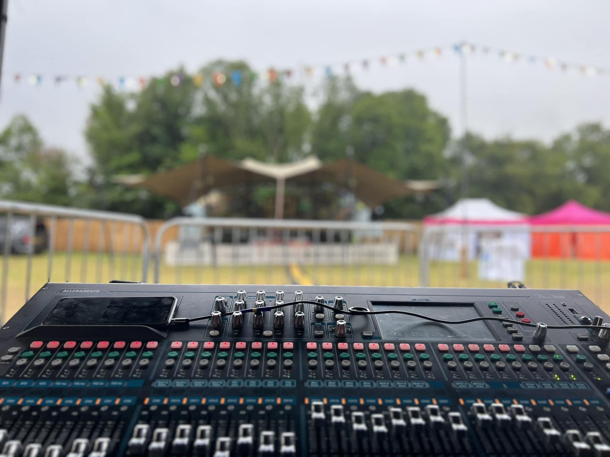 Front of house mixing desk set up at an outdoor festival field with bunting and marquees