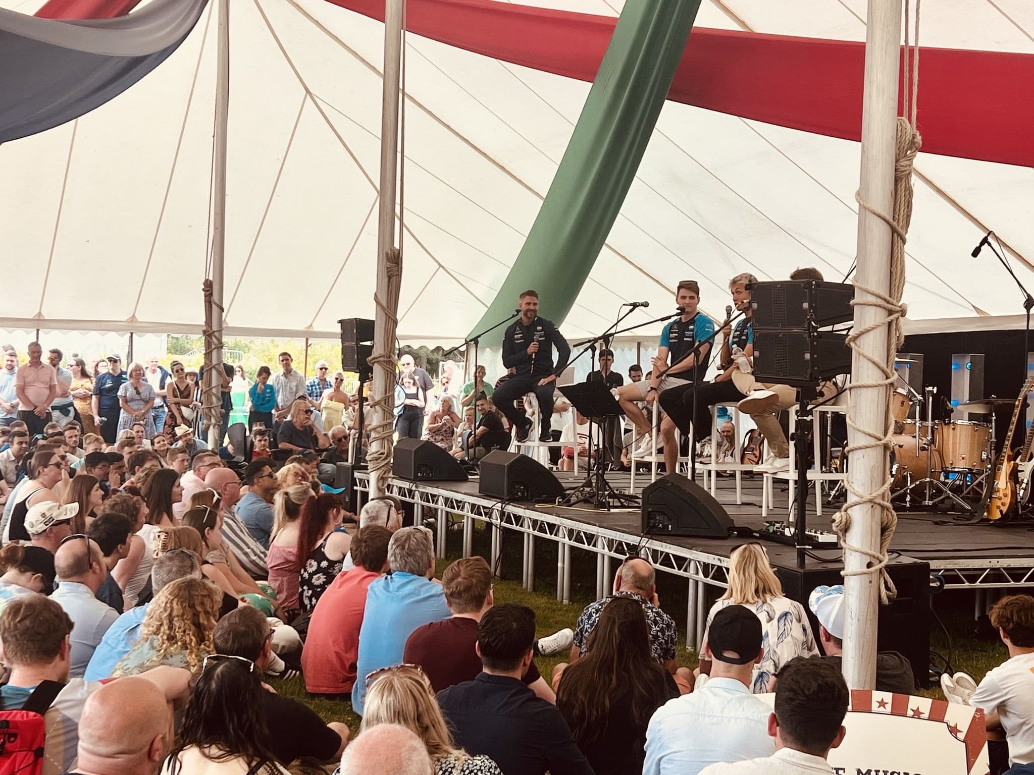 Seated audience watching an acoustic set on a stage inside a festival marquee