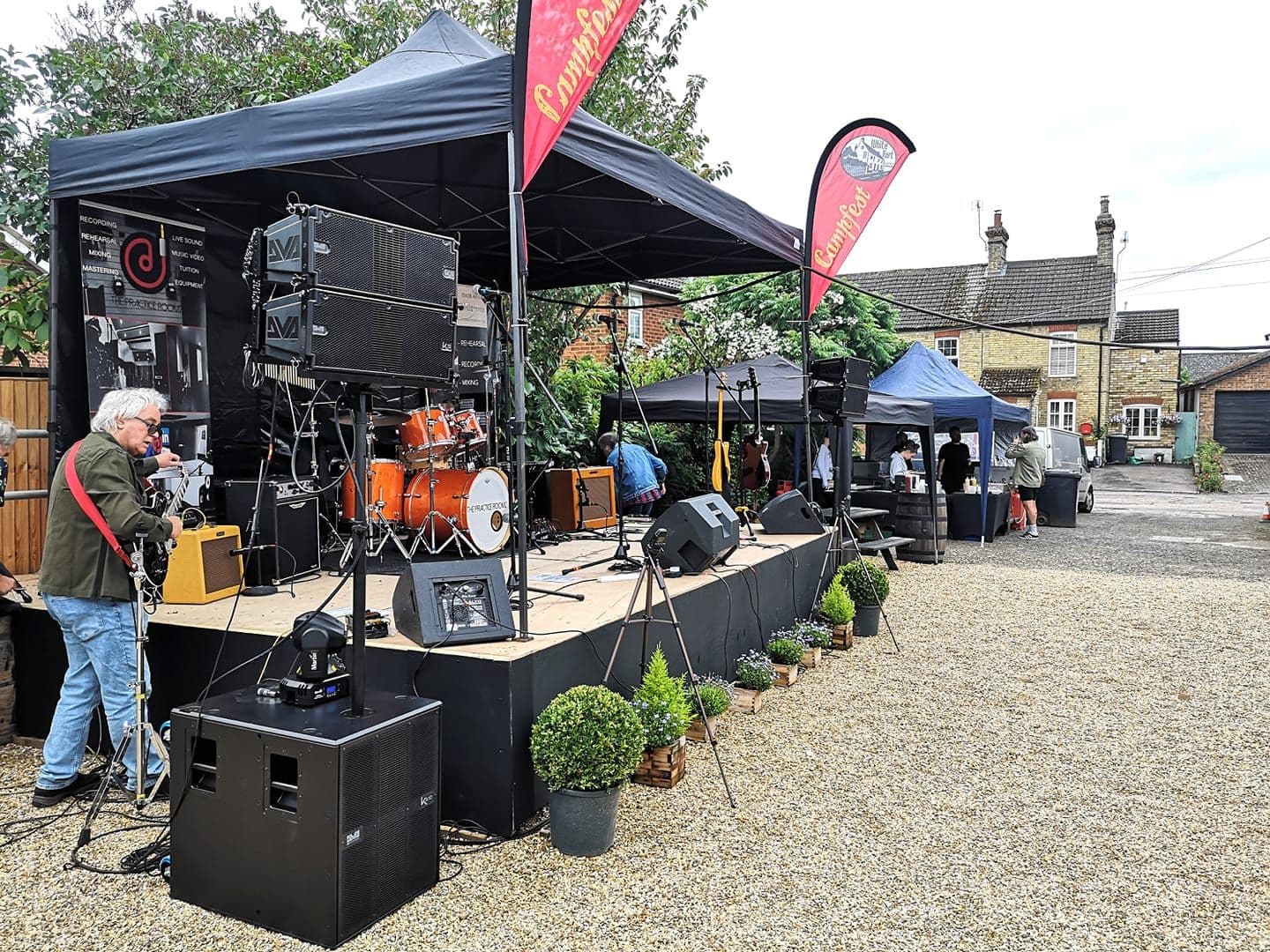Outdoor stage with PA speakers, subwoofers and a drum kit set up for a village music event